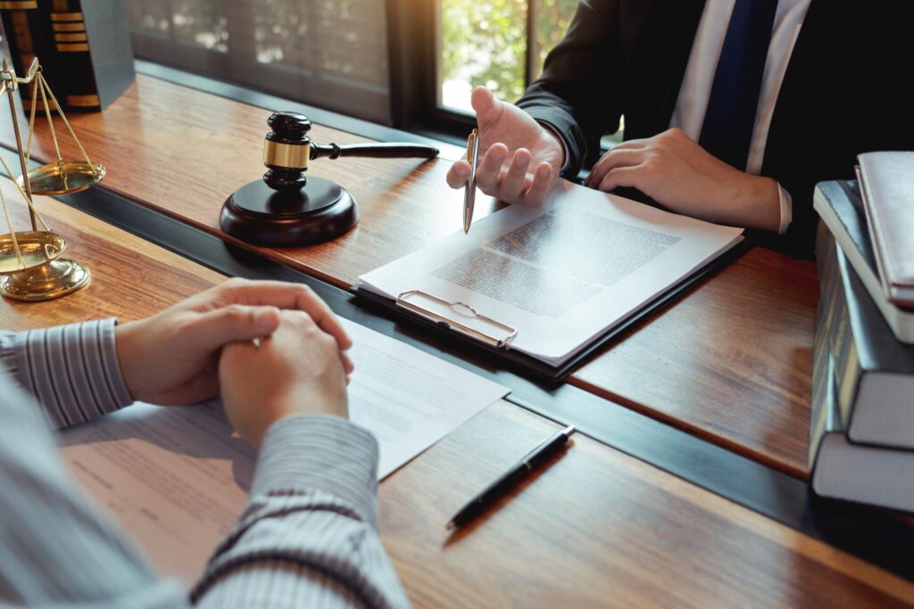 Two people sit at a desk discussing legal documents and paperwork with assault injury lawyers in a professional office setting featuring a gavel and scales.