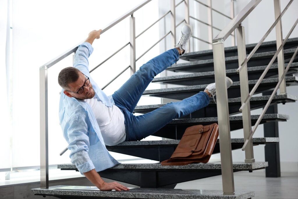A man in casual clothing falling backward on a staircase, an image used to illustrate how a slip and fall lawyer assists victims of premises liability accidents.