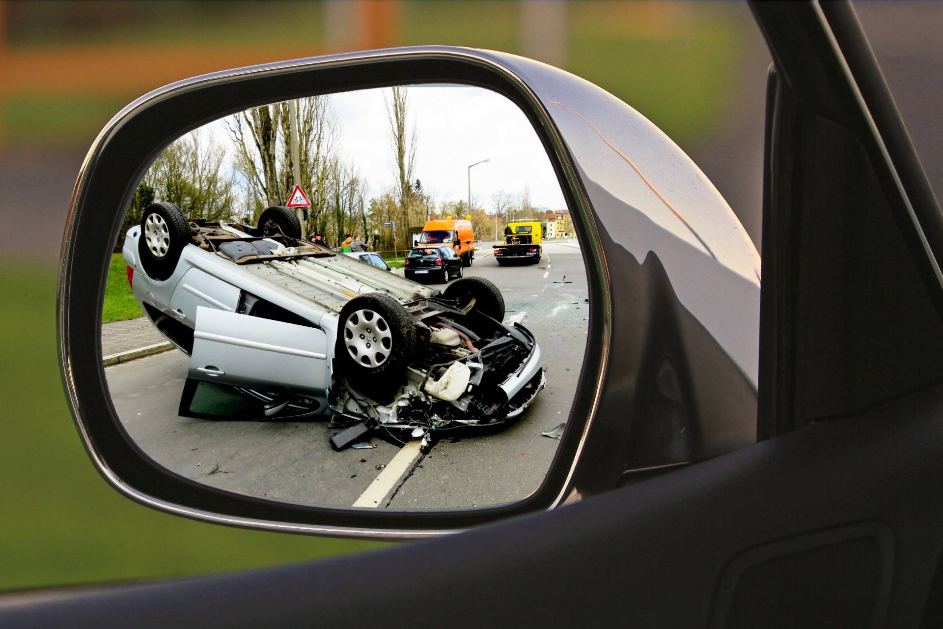 An overturned car is reflected in a side mirror with emergency vehicles at the scene, illustrating a case requiring a car wreck lawyer.