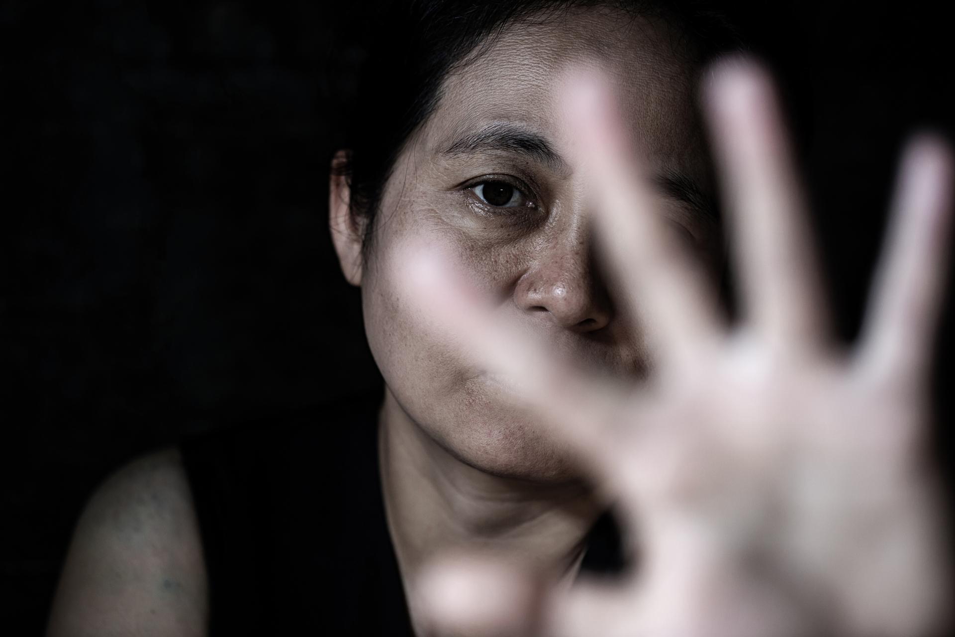 A person holds their hand up toward the camera, partially obscuring their face, with a serious expression and dark background—an image that echoes the determination of an Assault Injury Lawyer seeking justice.