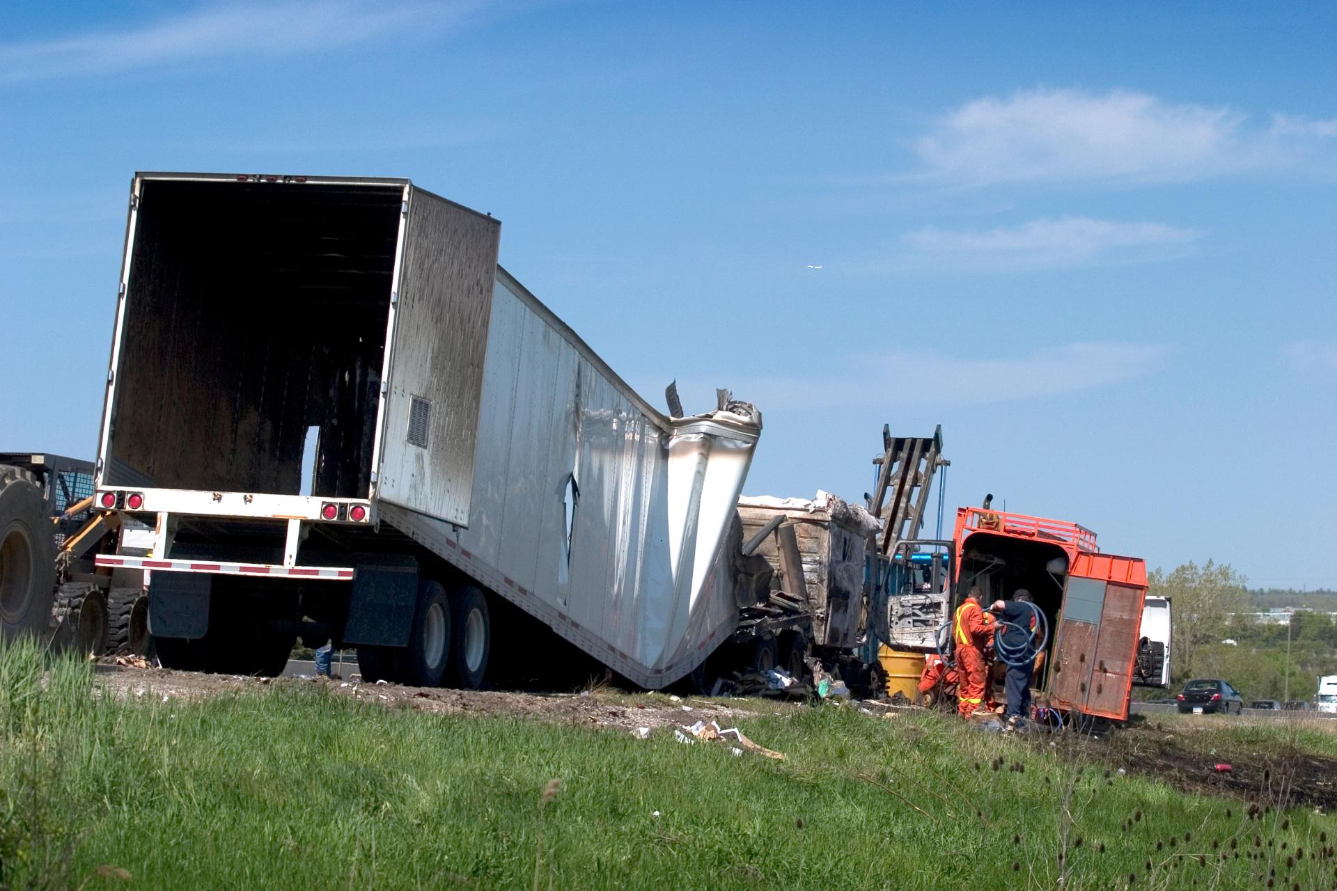 A semi-truck with a damaged trailer is off the road, with workers and a forklift nearby clearing debris—an incident where a Trucking Accident Lawyer could assist with claims.