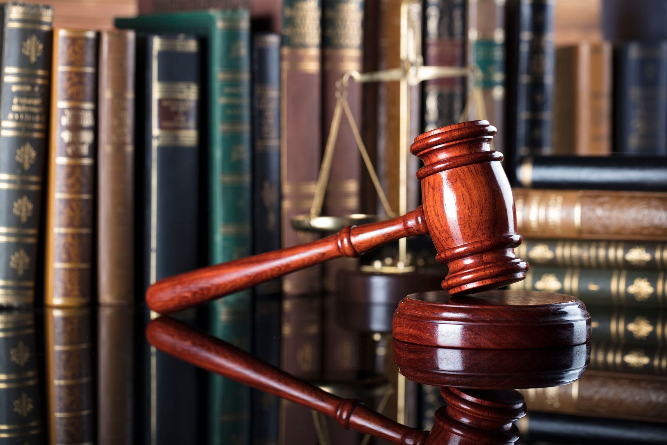 A wooden gavel rests on its sound block in front of a row of law books and a brass balance scale.