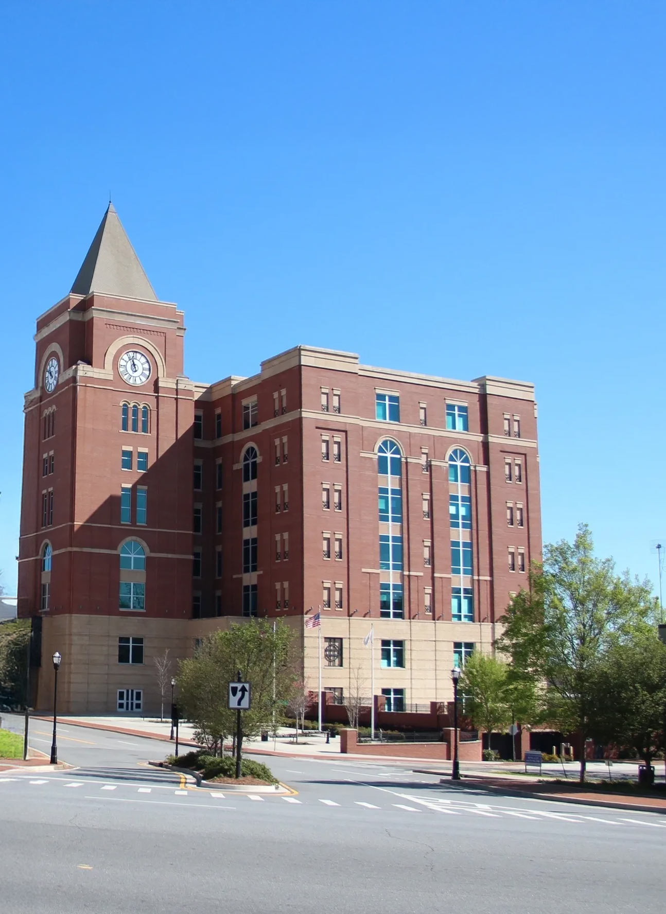 A large red brick courthouse with a clock tower and arched windows stands under a clear blue sky, marking one of the central service areas, with trees and a street in the foreground.