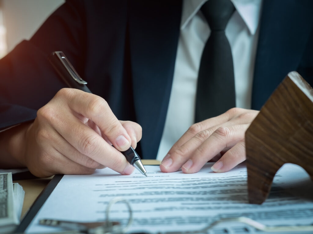 A person in a suit signs a document on a desk with a pen, next to a gavel and stack of cash—illustrating how insurance companies evaluate personal injury claims.