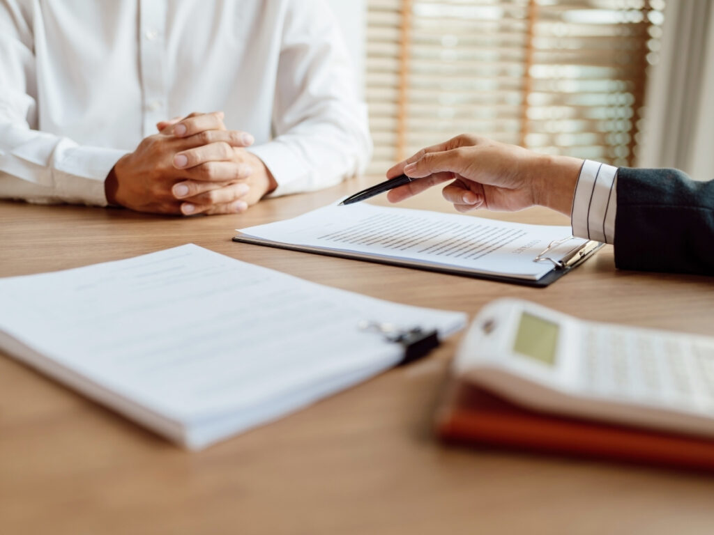 Two people sit at a desk with documents, a pen, and a calculator. One person points at a paper, suggesting a discussion about how insurance companies evaluate personal injury claims.