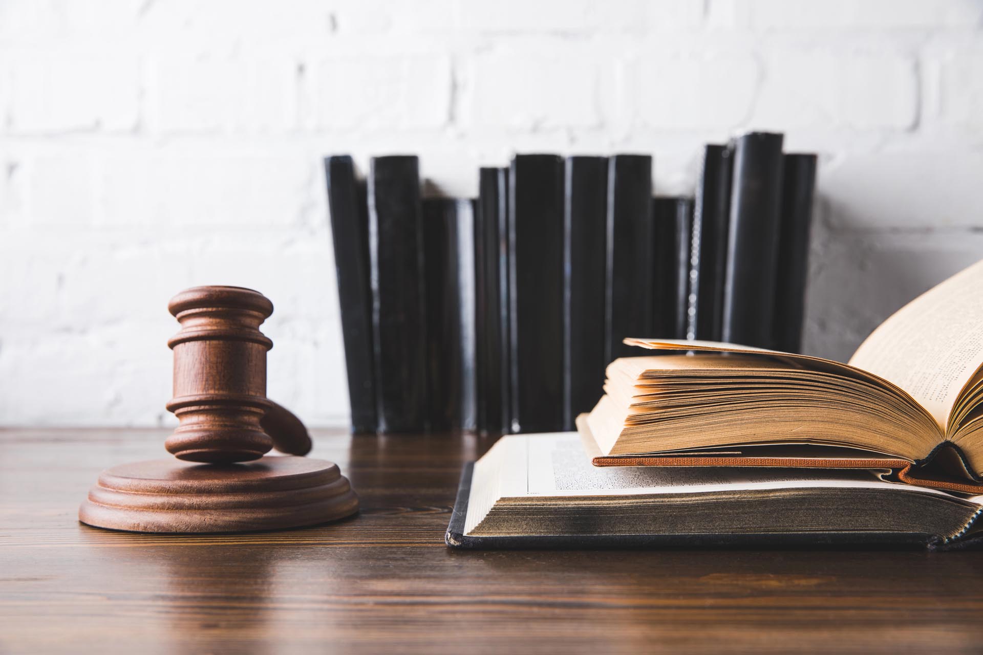 A wooden judge's gavel beside an open law book on a desk, with several closed books representing different practice areas standing upright in the background.
