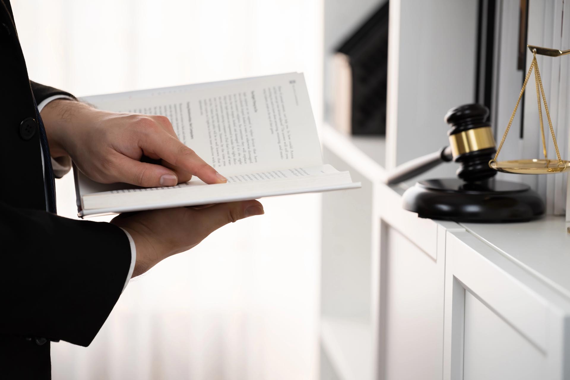 A person in a suit points to a page in an open book, with a gavel and scales of justice on a nearby shelf, highlighting different legal practice areas.