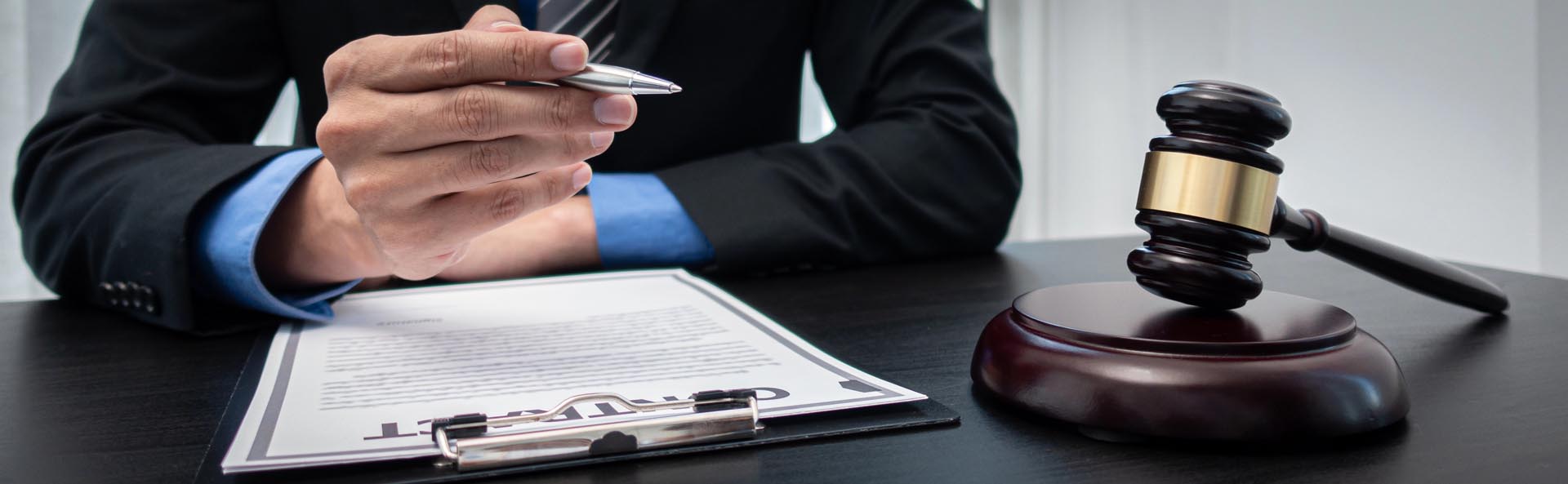 A person in a suit holding a pen reviews a contract on a clipboard, with a judge's gavel on the table nearby, highlighting legal practice areas.