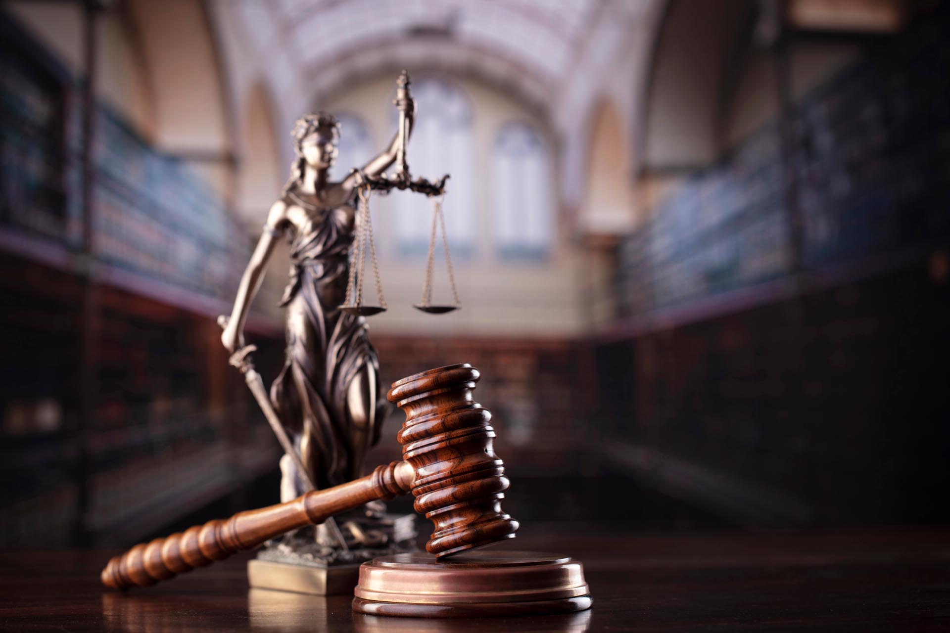 A judge's gavel rests on a sound block in front of a statue of Lady Justice, symbolizing the wide range of practice areas within the law, set in a library or courtroom setting.
