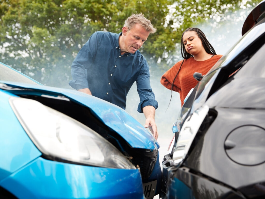 Two people examine the damage after a car accident involving a blue car and a black car, reflecting on what to do after a car accident in Georgia as they assess the visible dents on both vehicles.