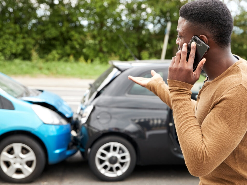 A man stands on the road making a phone call next to two cars involved in a rear-end collision, illustrating what to do after a car accident in Georgia.