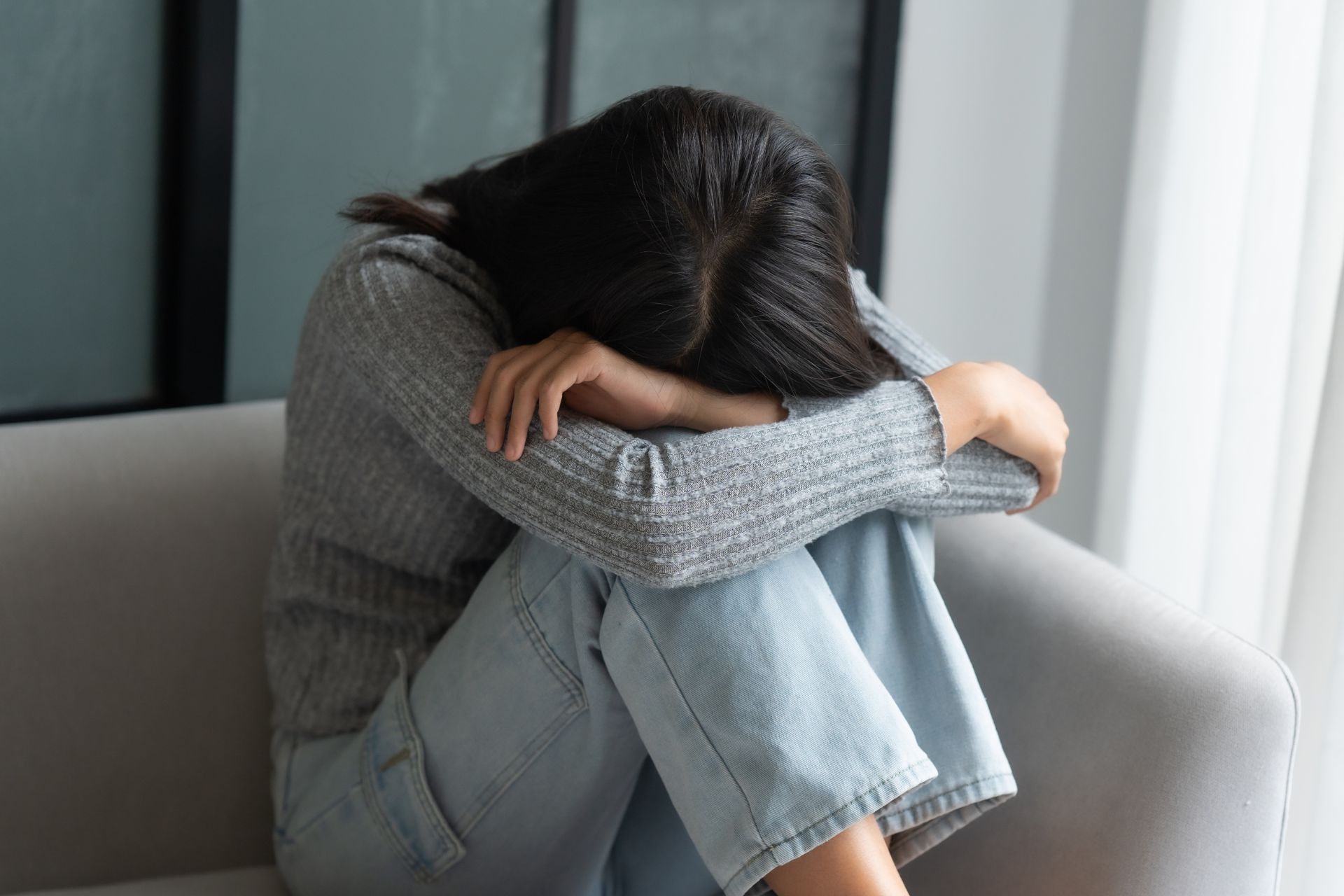 A person sits on a couch with knees drawn up and head resting on folded arms, appearing upset or distressed—perhaps seeking solace after consulting a wrongful death lawyer.