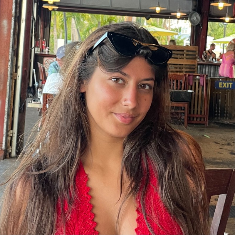 A woman with long brown hair wearing a red top and sunglasses on her head sits indoors at a restaurant, resembling the poised style often seen in an attorney bio.