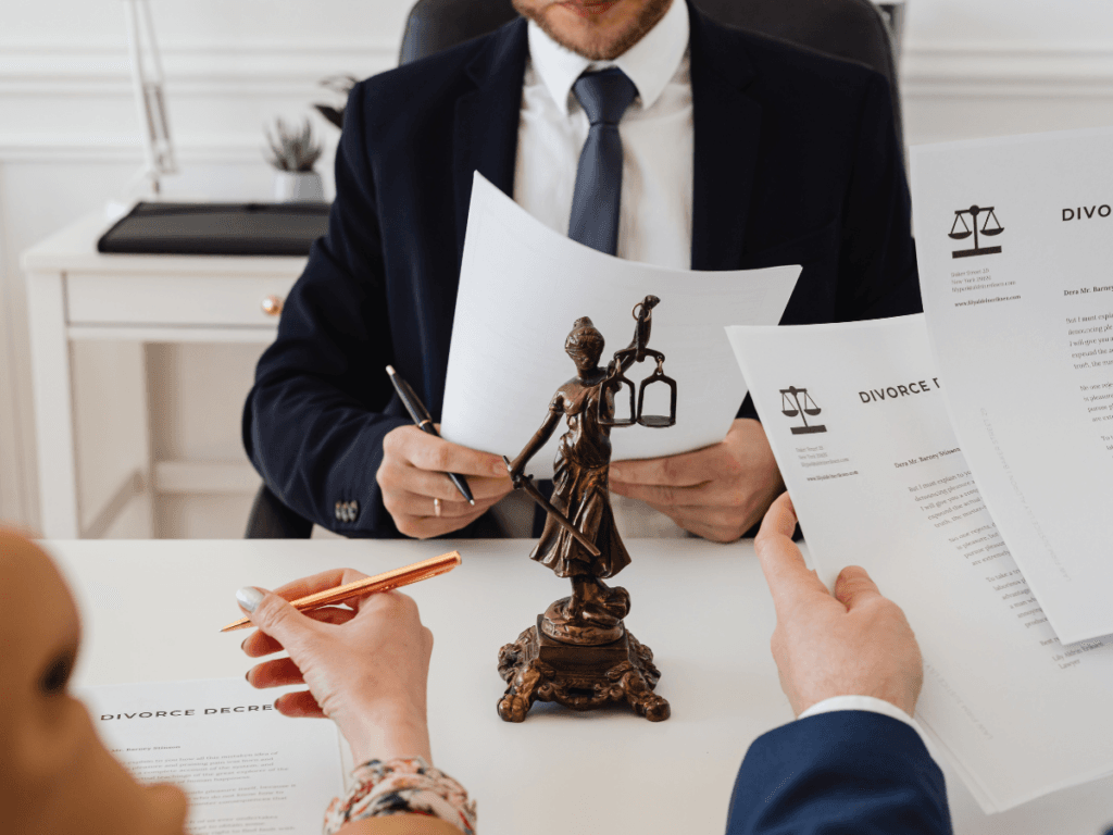Two people holding divorce decree documents sit across a desk from a lawyer in a suit—known for skilled Personal Injury Representation—with a small Lady Justice statue in the center.