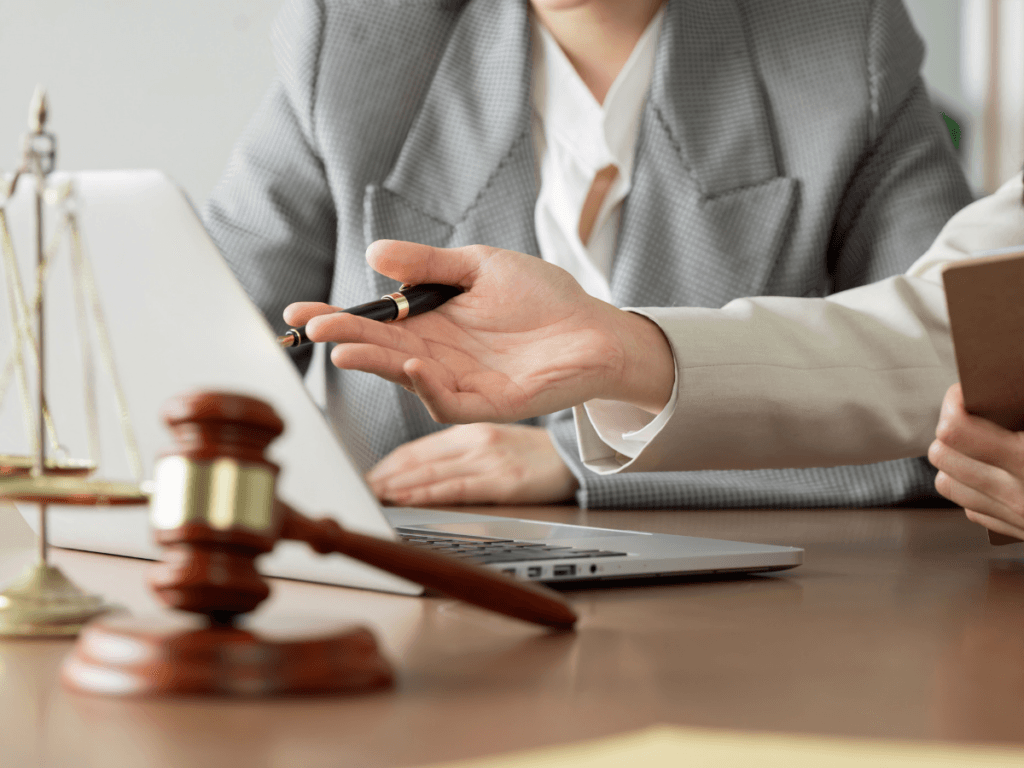 Two people in business attire discuss something on a laptop; a gavel and legal scales sit on the desk in the foreground, suggesting a consultation with a Personal Injury Lawyer in Georgia.