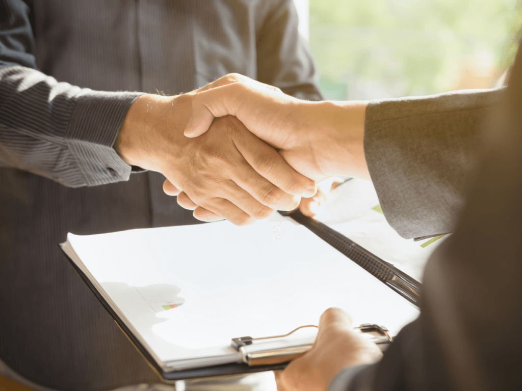 Two people shake hands over a clipboard with documents, suggesting a business agreement or partnership in a bright setting, as they make their Final Decision after taking time to Evaluate Settlement Options.