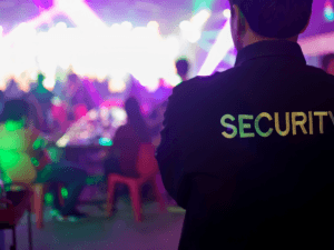 A security guard stands in the foreground at a crowded nightclub event in Georgia, with colorful lights and people sitting at tables in the background&mdash;a reminder of the importance of preventing negligent security incidents.